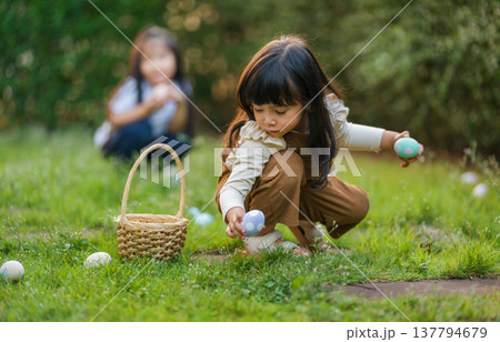two child girl playing together and hunting for Easter eggs into basket on green grass in garden two child girl playing together and hunting for Easter eggs into basket on green grass in garden 137794679