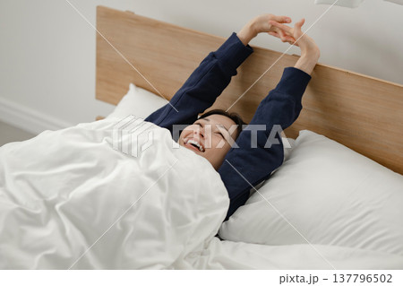 朝ベッドの上で伸びをする女性 137796502