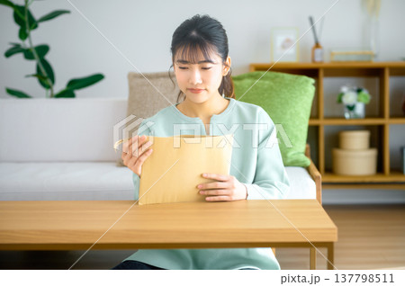 届いた重要書類や郵便物の封筒を開けて確認する女性 届いた重要書類や郵便物の封筒を開けて確認する女性 137798511