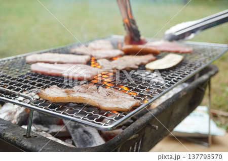 炭火で焼くバーベキューの網の上で肉やソーセージ、野菜を焼いているアウトドア料理のクローズアップ。 炭火で焼くバーベキューの網の上で肉やソーセージ、野菜を焼いているアウトドア料理のクローズアップ。 137798570