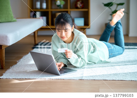 リビングでくつろぎながらノートパソコンでネットショッピングをする若い女性 137799103