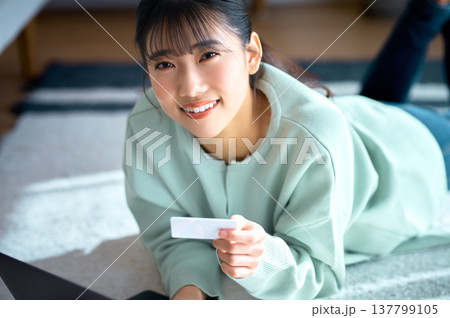 クレジットカードを持ち笑顔でカメラを見つめるネットショッピング中の若い女性 クレジットカードを持ち笑顔でカメラを見つめるネットショッピング中の若い女性 137799105