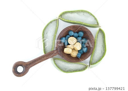 Aloe vera slices arranged around a wooden spoon filled with blue and yellow pills 137799421