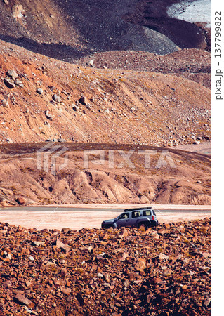A silver 4x4 vehicle driving through a rugged, rocky mountain valley near a riverbed. Extreme travel and exploration. A silver 4x4 vehicle driving through a rugged, rocky mountain valley near a riverbed. Extreme travel and exploration. 137799822