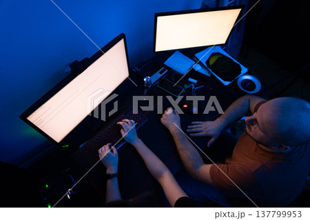 High angle view of a man and woman's hands on a keyboard and mouse in a dark workspace. High angle view of a man and woman's hands on a keyboard and mouse in a dark workspace. 137799953