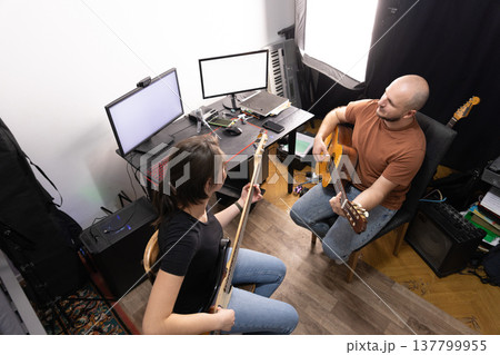 High angle shot of a male guitarist and female bassist rehearsing in a home music studio environment. High angle shot of a male guitarist and female bassist rehearsing in a home music studio environment. 137799955