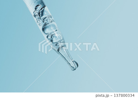 Dropper with clear serum liquid and bubbles on blue background, symbolizing hydration and beauty 137800334
