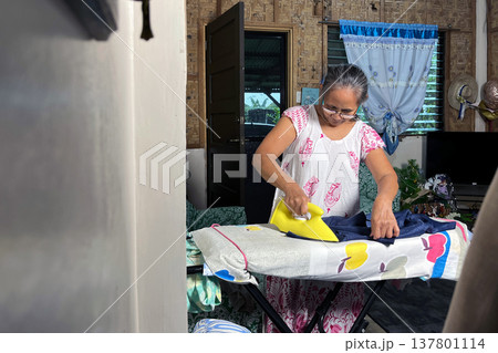 Senior woman ironing clothes on board in authentic home interior, elderly lady doing domestic chores, household routine portrait 137801114