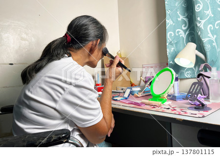 Senior woman sitting at desk and applying face powder with cosmetic brush, elderly lady doing makeup routine in her room Senior woman sitting at desk and applying face powder with cosmetic brush, elderly lady doing makeup routine in her room 137801115