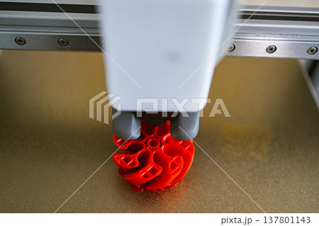 Close-up view of a 3D printer nozzle depositing molten plastic to create a complex red object layer by layer Close-up view of a 3D printer nozzle depositing molten plastic to create a complex red object layer by layer 137801143