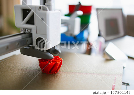 A close-up view of a 3D printer in action, meticulously building a vibrant red object layer by layer on its build plate 137801145