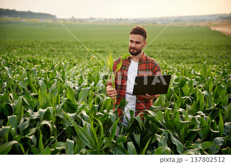Big laptop and corn in hands. Man is on the agricultural field Big laptop and corn in hands. Man is on the agricultural field 137802512