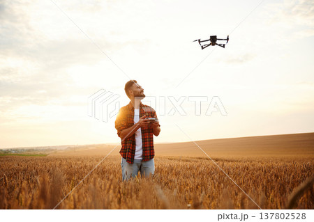 Looking at the drone, controlling it. Male farmer is on the wheat agricultural field Looking at the drone, controlling it. Male farmer is on the wheat agricultural field 137802528