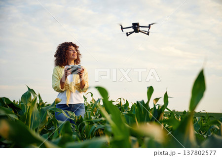 Little help from a drone, controlling it. Woman is on the corn agricultural field Little help from a drone, controlling it. Woman is on the corn agricultural field 137802577