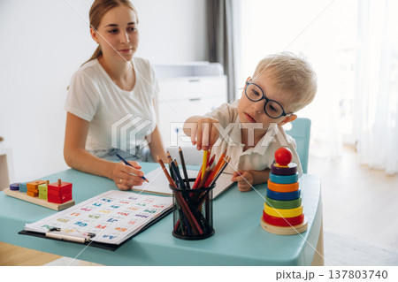 Trying to learn how to draw, holding pencil. Speech therapist is with young boy indoors 137803740