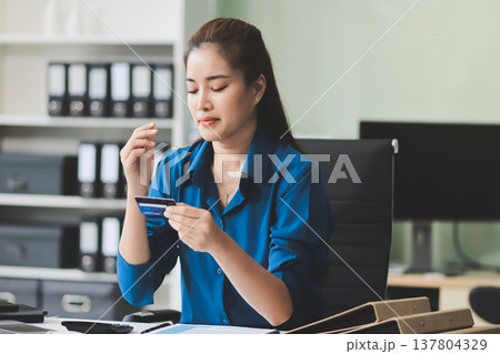Young businesswoman is holding two credit cards with a worried expression, trying to decide which one to use to pay off her debt 137804329