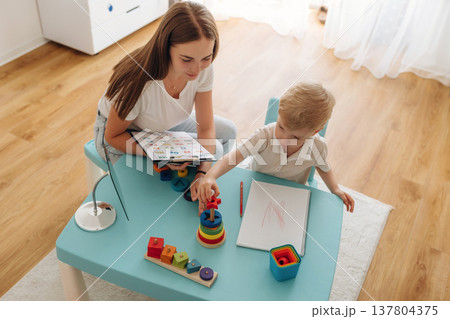 Tasks for motor skills and logic. Speech therapist is with young boy indoors 137804375