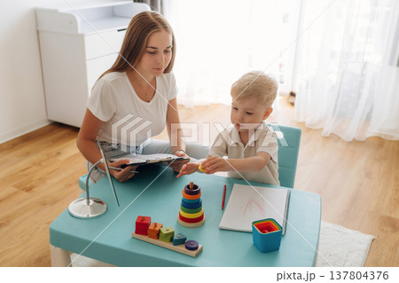 Tasks for motor skills and logic. Speech therapist is with young boy indoors Tasks for motor skills and logic. Speech therapist is with young boy indoors 137804376