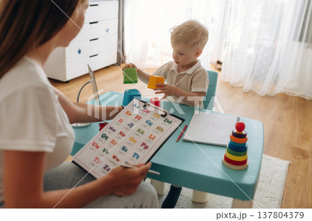 Tasks for motor skills and logic. Speech therapist is with young boy indoors Tasks for motor skills and logic. Speech therapist is with young boy indoors 137804379