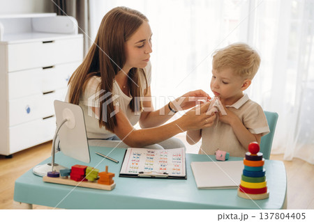 By the blue table. Speech therapist is with young boy indoors By the blue table. Speech therapist is with young boy indoors 137804405