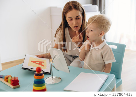 The right way to pronounce the letters. Speech therapist is with young boy indoors The right way to pronounce the letters. Speech therapist is with young boy indoors 137804415