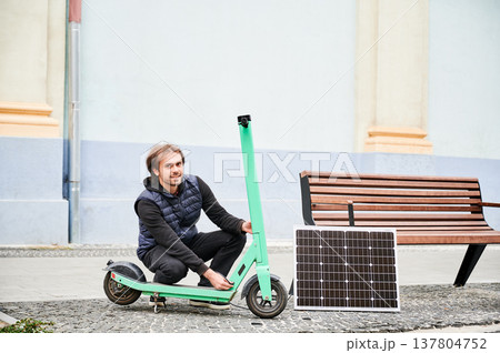 Man connects solar panel to electric scooter for charge. Integration of solar power as sustainable energy source for charging electric scooters, promoting eco-friendly urban transportation. Man connects solar panel to electric scooter for charge. Integration of solar power as sustainable energy source for charging electric scooters, promoting eco-friendly urban transportation. 137804752