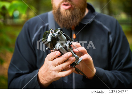 In a lush forest, a bearded man holds a modern device, sharing excitement about technology. Sunlight filters through the trees, enhancing the experience of discovery. In a lush forest, a bearded man holds a modern device, sharing excitement about technology. Sunlight filters through the trees, enhancing the experience of discovery. 137804774