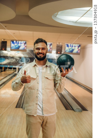 Showing the ball, standing. Man is playing bowling indoors 137804918