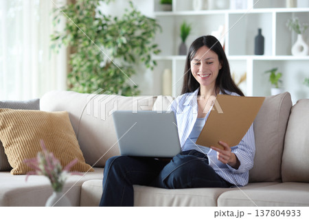 Happy asian woman comparing paper documents online 137804933