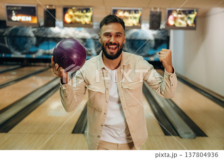 Celebrating, smiling and holding the ball. Man is playing bowling indoors Celebrating, smiling and holding the ball. Man is playing bowling indoors 137804936