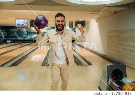 Celebrating, smiling and holding the ball. Man is playing bowling indoors Celebrating, smiling and holding the ball. Man is playing bowling indoors 137804938
