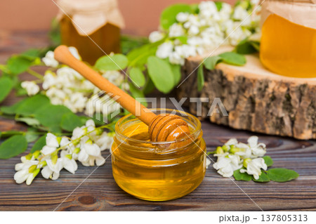 Sweet honey jar surrounded spring acacia blossoms. Honey flows from a spoon in a jar. jars of clear fresh acacia honey on wooden background 137805313