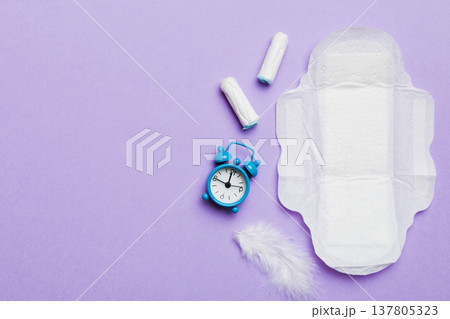 Ringing alarm clock with sanitary female tampons and menstrual sanitary pads. Medical concept of woman critical days and menstruation. Female daily hygiene. Copy space 137805323