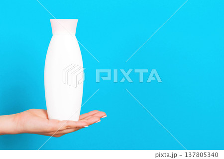 Female hand holding cream bottle of lotion isolated. Girl give tube cosmetic products on blue background Female hand holding cream bottle of lotion isolated. Girl give tube cosmetic products on blue background 137805340
