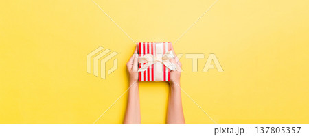 Woman arms holding gift box with colored ribbon on yellow table background, top view and copy space for you design Woman arms holding gift box with colored ribbon on yellow table background, top view and copy space for you design 137805357