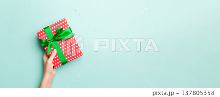 Woman hands give wrapped christmas or other holiday handmade present in colored paper. Present box, decoration of gift on Blue table, top view with copy space Woman hands give wrapped christmas or other holiday handmade present in colored paper. Present box, decoration of gift on Blue table, top view with copy space 137805358