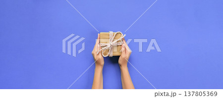 Woman hands give wrapped valentine or other holiday handmade present in paper with pink ribbon. Present box, decoration of gift on table, top view with copy space Woman hands give wrapped valentine or other holiday handmade present in paper with pink ribbon. Present box, decoration of gift on table, top view with copy space 137805369