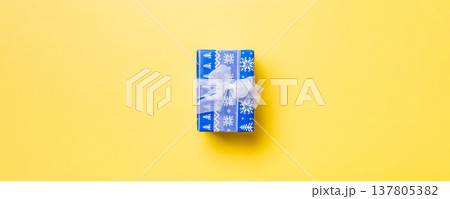 wrapped Christmas or other holiday handmade present in paper with white ribbon on yellow background. Present box, decoration of gift on colored table, top view with copy space 137805382