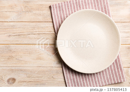 Top view on colored background empty round white plate on tablecloth for food. Empty dish on napkin with space for your design Top view on colored background empty round white plate on tablecloth for food. Empty dish on napkin with space for your design 137805413