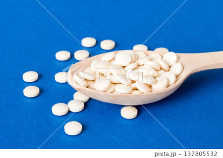Heap of white pills on colored background. Tablets scattered on a table. Pile of red soft gelatin capsule. Vitamins and dietary supplements concept Heap of white pills on colored background. Tablets scattered on a table. Pile of red soft gelatin capsule. Vitamins and dietary supplements concept 137805532
