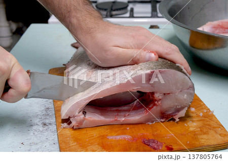 Man prepares fresh silver carp fish. Cuts it into steaks with a knife. home cooking concept Man prepares fresh silver carp fish. Cuts it into steaks with a knife. home cooking concept 137805764