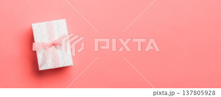 wrapped Christmas or other holiday handmade present in paper with pink ribbon on living coral background. Present box, decoration of gift on colored table, top view with copy space wrapped Christmas or other holiday handmade present in paper with pink ribbon on living coral background. Present box, decoration of gift on colored table, top view with copy space 137805928