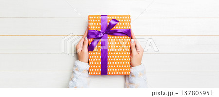 Top view woman hands holding present box with colored bow on white wooden background with copy space Top view woman hands holding present box with colored bow on white wooden background with copy space 137805951
