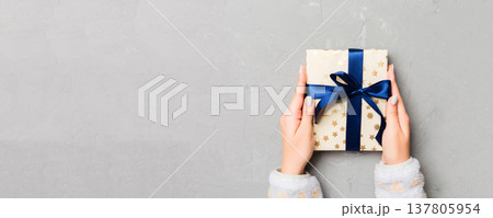 Flat lay of woman hands holding gift wrapped and decorated with bow on gray cement wooden background with copy space. Christmas and holiday concept Flat lay of woman hands holding gift wrapped and decorated with bow on gray cement wooden background with copy space. Christmas and holiday concept 137805954