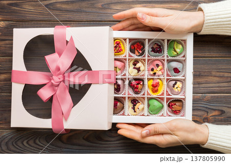Female hands with delicious candies in box on color background Female hands with delicious candies in box on color background 137805990