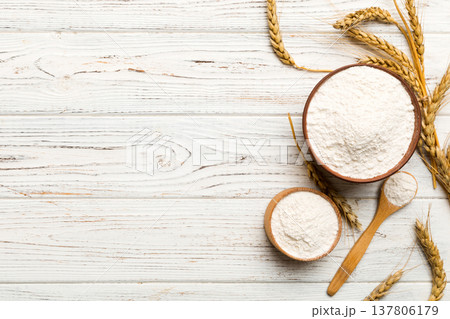 Flat lay of Wheat flour in wooden bowl with wheat spikelets on colored background. world wheat crisis Flat lay of Wheat flour in wooden bowl with wheat spikelets on colored background. world wheat crisis 137806179