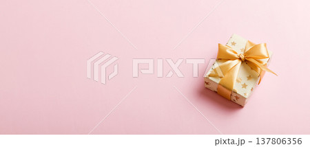 wrapped Christmas or other holiday handmade present in white paper with gold ribbon on colored background. Present box, decoration of gift on colored table, top view with copy space wrapped Christmas or other holiday handmade present in white paper with gold ribbon on colored background. Present box, decoration of gift on colored table, top view with copy space 137806356
