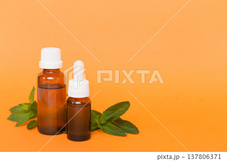 Natural Mint Essential Oil in a Glass Bottle. organic cosmetics with herbal extracts of mint on colored background Natural Mint Essential Oil in a Glass Bottle. organic cosmetics with herbal extracts of mint on colored background 137806371