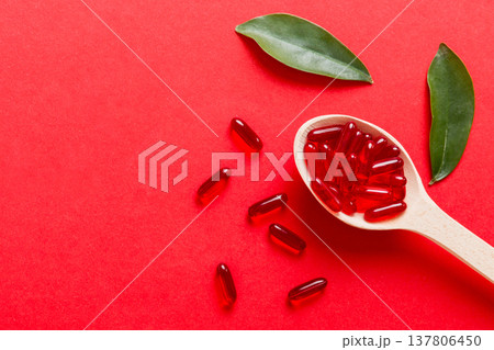 Vitamin capsules in a spoon on a colored background. Pills served as a healthy meal. Red soft gel vitamin supplement capsules on spoon Vitamin capsules in a spoon on a colored background. Pills served as a healthy meal. Red soft gel vitamin supplement capsules on spoon 137806450