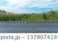 Horizontal or Landscape view of asphalt road. Side of road with footpath with beautifully manicured grass. Background of dense overgrown grass under blue sky and white clouds. 137807419